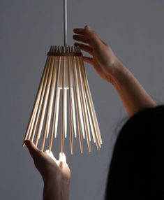 a woman is holding up a light fixture made out of bamboo sticks and wood dows