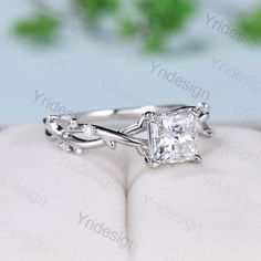 a white gold ring with a princess cut diamond in the center and vines on each side