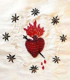 an embroidered heart surrounded by black and red flowers on a white linen background with starbursts