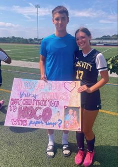 two people standing on a soccer field holding a sign