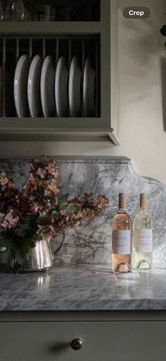 a bottle of wine sitting on top of a counter next to a vase filled with flowers