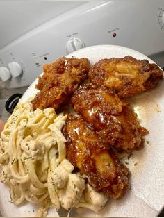 a white plate topped with pasta and chicken wings next to a pile of noodles on top of a dryer