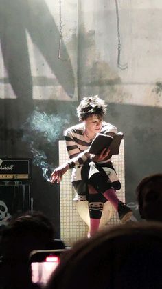 a man sitting on top of a white chair in front of a microphone while holding a book