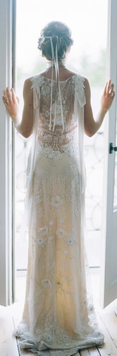 a woman standing in front of a door wearing a wedding dress with sheer lace on it