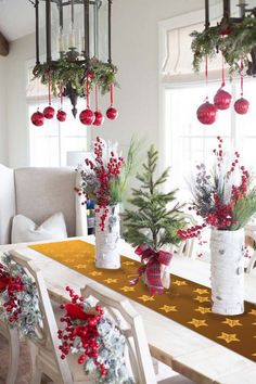 a dining room table decorated for christmas with red ornaments and greenery in vases