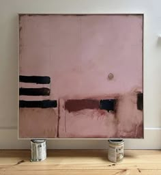 two cans of paint sitting on top of a wooden table next to a pink painting