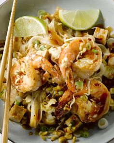 a plate with shrimp, noodles and limes next to chopsticks