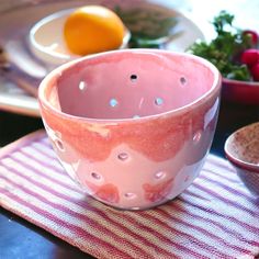 a pink bowl sitting on top of a table next to plates and bowls filled with fruit