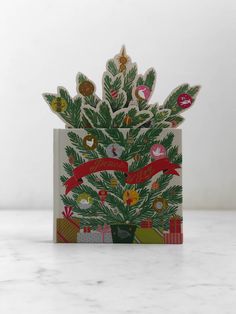 a christmas card with an image of a pine tree and presents on the front, in red ribbon