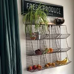 a metal rack with fruit and vegetables hanging on the wall next to a green curtain