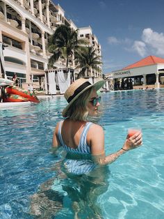 a woman in a hat holding an orange frisbee while standing in a swimming pool