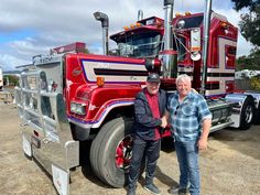 two men standing next to a large red truck