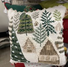 a decorative pillow with trees and houses on it in front of a pile of pillows