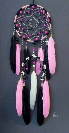 a pink and black dream catcher hanging from a hook on a gray wall with beads