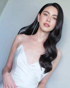 a woman with long black hair wearing a white dress and holding her hand on her hip