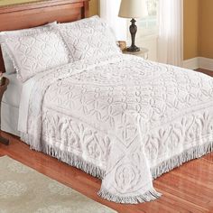 a white bedspread with fringe trim on it in a bedroom next to a lamp