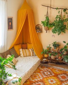 a bed with a yellow canopy over it in a room filled with potted plants