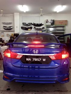 the back end of a blue honda car parked in a garage with other cars behind it