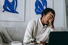 a man sitting on a couch with his head in his hands while using a laptop