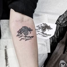 a person with a tattoo on their arm has an eye in the sky and clouds