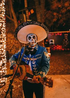 a man wearing a skeleton face paint playing a guitar in front of a tree with christmas lights