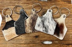 three cow hide keychains are shown on a wooden surface, one is black, the other is white and brown