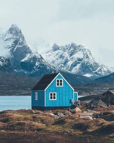 a small blue house sitting on top of a grass covered field next to snow covered mountains