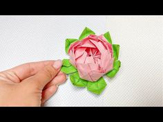 someone is making a paper flower out of green and pink origami pieces on a white surface