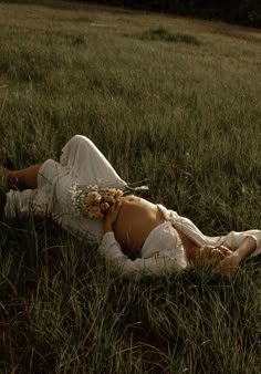 a woman is laying in the grass with flowers on her head and body, wearing a white dress