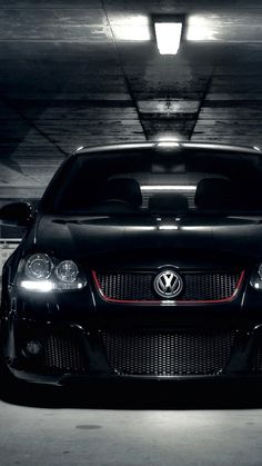 the front end of a black car in a parking garage with its lights turned on