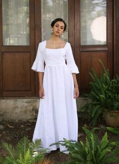 a woman standing in front of a door wearing a white dress with puffy sleeves