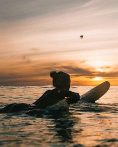 a person laying on a surfboard in the ocean at sunset with a bird flying overhead