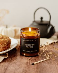 an autumn night candle next to a muffin on a plate with a tea kettle in the background