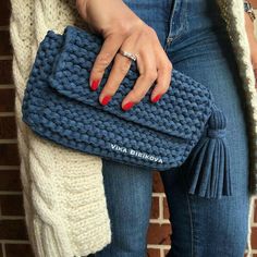 a woman is holding a blue knitted clutch bag in front of a brick wall