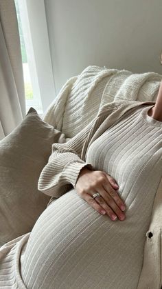 a pregnant woman laying on top of a bed next to a white window sill