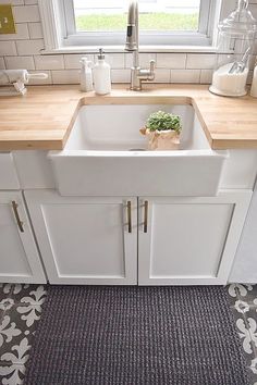 a white kitchen sink sitting under a window in front of a counter top with a potted plant on it