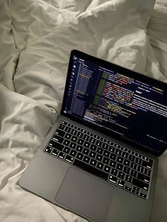 an open laptop computer sitting on top of a white bed covered in sheets and pillows