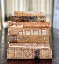 a stack of old books sitting on top of a wooden table next to a window