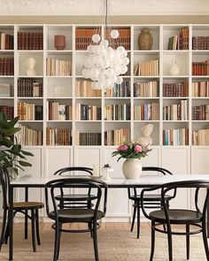 a dining room table and chairs in front of bookshelves with vases on them