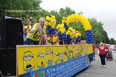 a group of people riding on the back of a yellow and blue float with balloons