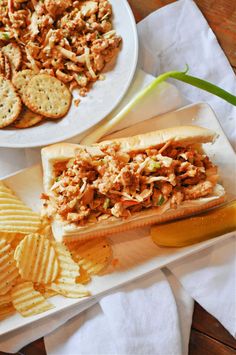 there is a sandwich and chips on the plate next to each other, along with a bowl of crackers