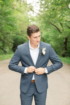 a man in a blue suit and white shirt is standing on the road with his hands behind his back