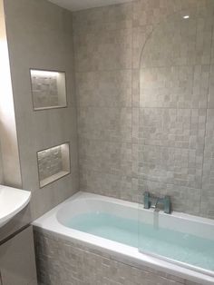 a bath tub sitting next to a white sink in a bathroom under a mirror with lights on it