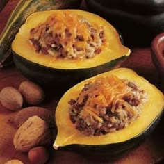 two squash halves filled with meat and cheese on top of a wooden table next to nuts