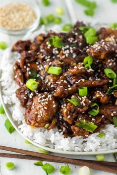 a white plate topped with rice covered in meat and green onions next to chopsticks