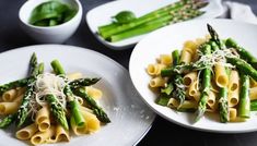 two white plates with pasta and asparagus on them