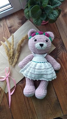 a crocheted teddy bear in a white dress next to a plant and envelope