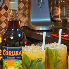 two glasses filled with drinks sitting on top of a table next to bottles of alcohol