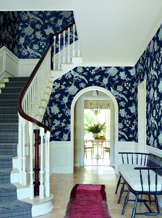 an entry way with blue and white wallpaper on the walls, carpeted stairs and table