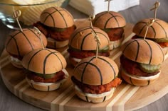 small sandwiches are arranged on a cutting board with toothpicks stuck in the buns